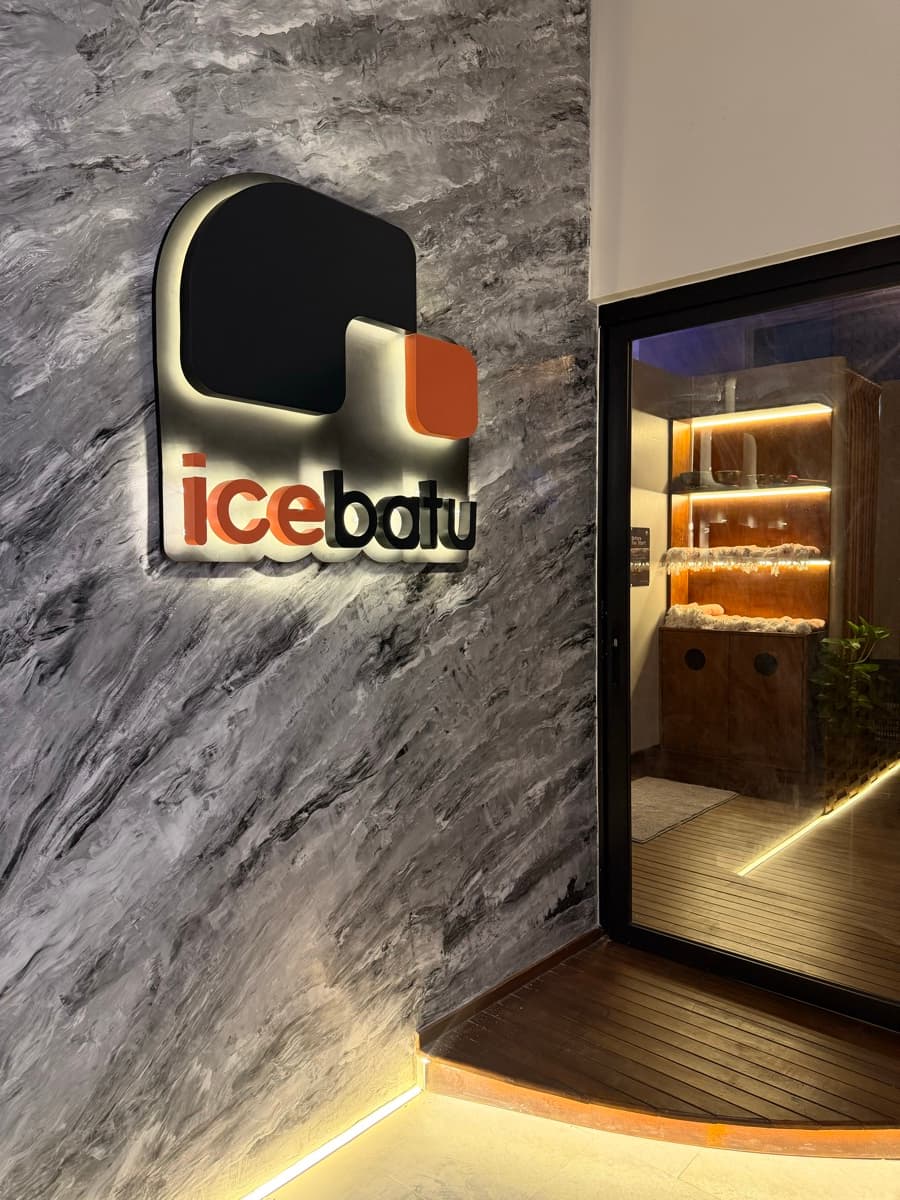 The icebatu logo lit on the marble entrance wall, sauna beyond